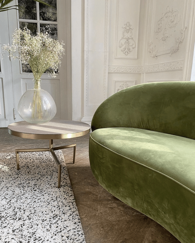 pale lime green sofa and brass coffee table with a vase of small white flowers in foreground of a white gothic style paneled wall